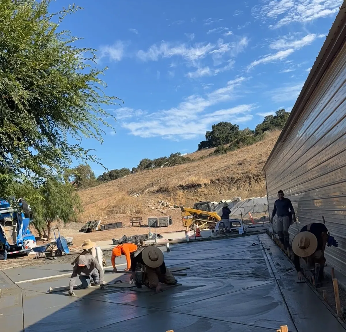 Crew finishing a large concrete slab beside a metal building